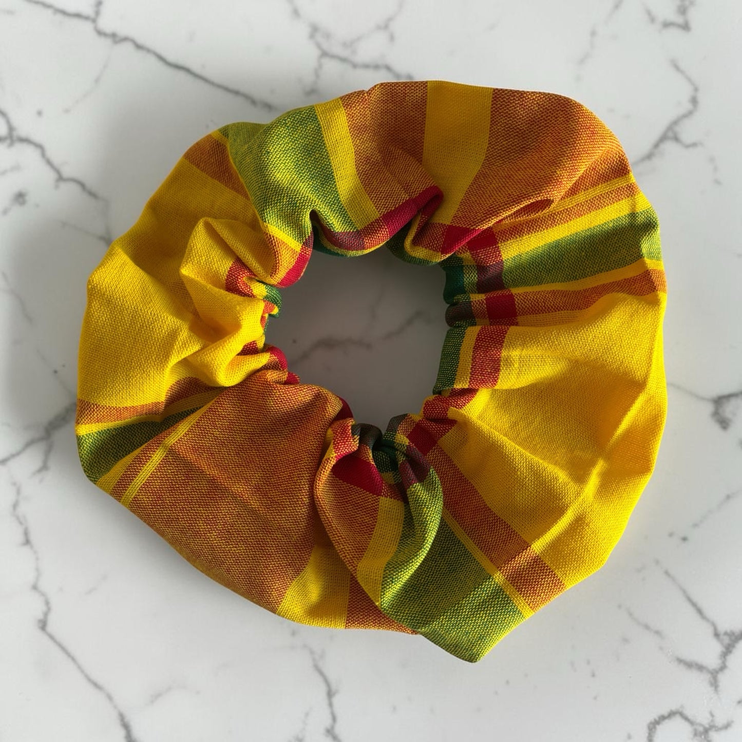 Chouchou LillyCreation en tissu madras traditionnel à carreaux jaunes, verts et rouges sur fond marbré.